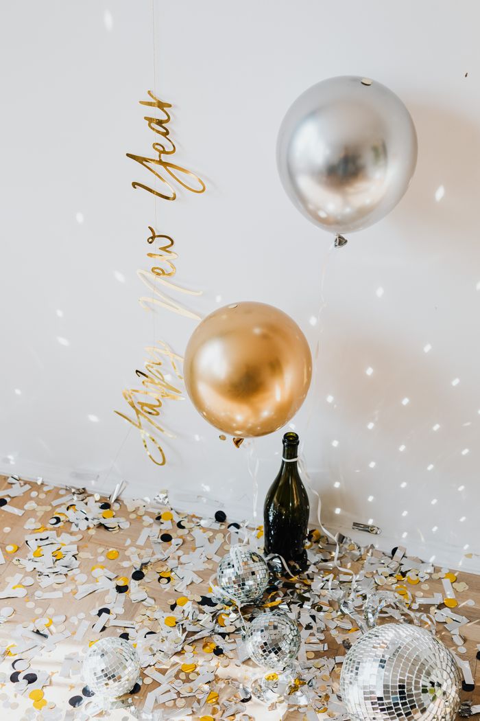 Festive scene featuring balloons, confetti, and a champagne bottle for New Year celebration.